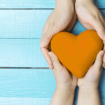 Hands holding a heart against a teal wall background